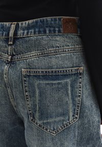 Vaqueros de denim azul claro con corte recto, con costuras naranjas, una etiqueta de cuero en la cinturilla y bolsillos traseros.