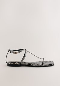 Platte sandaal met zwart-wit slangenprint, dunne bandjes en een kleine gesp rond de enkel, weergegeven op een effen achtergrond.