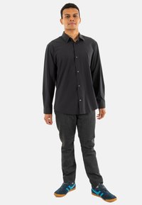 Camisa de botones de manga larga negra, de tela suave, combinada con jeans oscuros y zapatillas azules con toques turquesa y suela de goma.