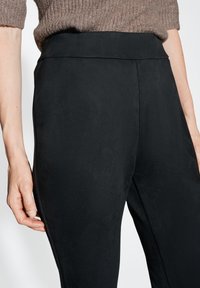 Pantaloni neri aderenti in un tessuto liscio e testurizzato. Presentano una vita alta e un dettaglio sulla cucitura laterale, mostrando una silhouette elegante.