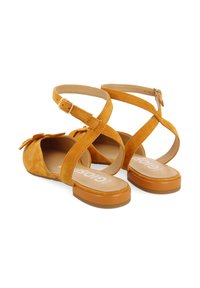 Sandalias amarillas de ante con diseño de tiras cruzadas y hebilla ajustable en el tobillo. Plantilla texturizada y suela de goma plana con una ligera plataforma.