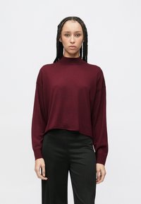 Bluză burgund cu mâneci lungi, guler tip mocă, croială lejeră și textură moale. Asortată cu pantaloni negri croiți, cu dungi fine și subtile.