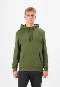 Olive green hoodie made of soft fabric with a kangaroo pocket, drawstrings, ribbed cuffs, and hem; worn with dark gray pants.