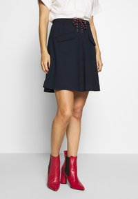 Marinblå dragsko kjol med två framfickor, tillverkad av ett mjukt material. Matchad med röda ankelboots med hög klack.