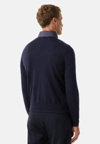 Pull en tricot bleu marine avec un ourlet et des poignets côtelés, doté d'un col contrastant. Texture lisse et coupe ajustée, présenté de dos.