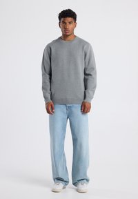 Gray sweatshirt with a round neckline, long sleeves, and ribbed cuffs, paired with light blue wide-leg jeans and white sneakers.