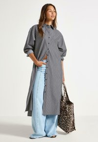 Svart och vit randig skjortklänning med knappstängning, långa ärmar och sidofickor, kombinerad med ljusblå vida jeans och en väska med leopardmönster.