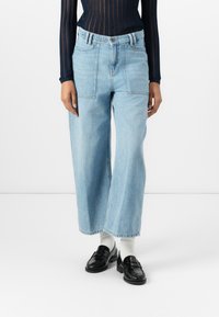 Jeans a gamba larga di un azzurro chiaro realizzati in denim, con vita alta, cuciture a contrasto e due tasche frontali. Abbinati a mocassini neri.