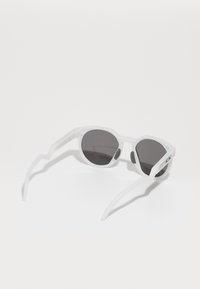 Gafas de sol blancas sin montura con lentes oscuros, diseño angular, brazos texturizados y almohadillas nasales de goma gris. Adecuadas para uso deportivo.