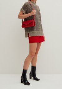 Braun und schwarz gestricktes Kurzarmoberteil, rote Shorts, rote Handtasche, schwarze Stiefeletten mit Absatz, glatter Textur und glänzendem Finish.