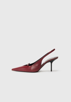 Red leather slingback heels with a pointed toe, open side, and a slim high heel. Features a small loop accent at the front.