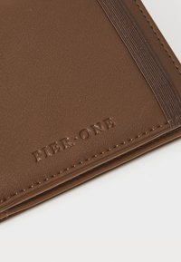 Cartera de cuero marrón con una superficie texturizada, presenta bordes cosidos y el logo en relieve "PIER ONE" en un diseño sutil.