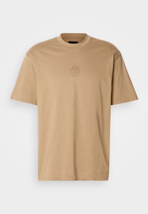 Beiges Baumwoll-T-Shirt mit rundem Ausschnitt, kurzen Ärmeln und einem geprägten Logodetail auf der Brust. Lockerer Schnitt mit glatter Textur.