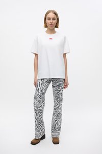 Witte katoenen t-shirt met rood logo, gecombineerd met grijs flared broek met zebra patroon. Model draagt bruine hoge laarzen.