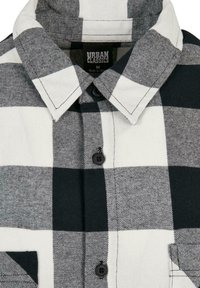 Svart og hvit rutete skjorte med krage, knapper og brystlomme, laget av teksturert stoff. Merket leser "Urban Classics."