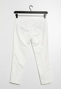 Witte broek hangt aan een zwarte hanger, met een slim fit, gladde stof, twee achterzakken en een strakke, geklede uitstraling.