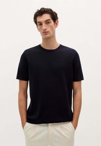 Mørkeblå kortærmet t-shirt lavet af et glat materiale, med en rund halsudskæring og en afslappet pasform, båret med lyse bukser.