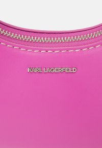 Surface en cuir rose vif avec fermeture éclair argentée et détails cousus, avec texte du logo Karl Lagerfeld en argent.
