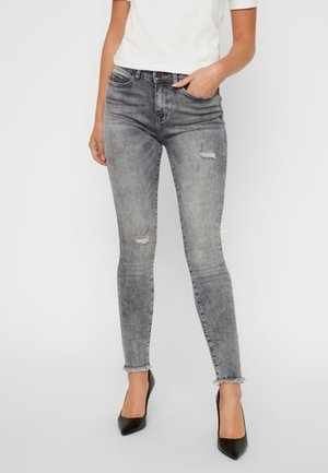 Jeans skinny de mezclilla gris con detalles desgastados, cinturilla de altura media y silueta ajustada, combinados con tacones altos negros.