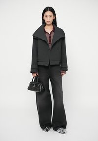 Sort oversize uldjakke med bred krave, kombineret med en bordeaux polo og sorte jeans med vide ben, holder en lille sort håndtaske.