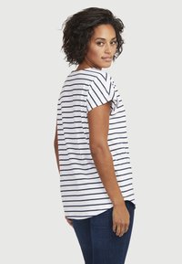 Raidallinen puuvillateepaita, jossa on lyhyet hihat ja pyöreä helma. Paita on pääasiassa valkoinen tummansinisillä raidoilla ja se on yhdistetty tummaan farkkuihin.