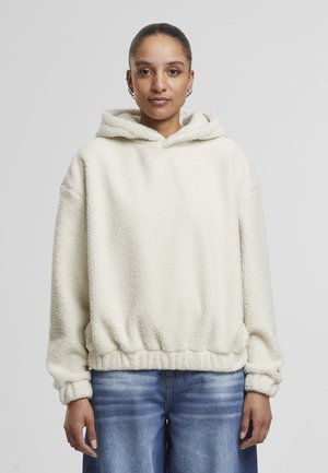 Un sweat à capuche en polaire crémeux et moelleux avec un cordon de serrage, un ourlet élastique et des manches à poignet. Porté sur un jean en denim bleu à jambes larges.