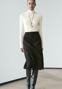 Light beige turtleneck, fitted, paired with a high-waisted black skirt. Long black boots with a glossy finish, minimalistic silver necklace accent.