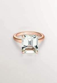 Anillo de oro rosa que presenta una gran piedra de corte esmeralda clara con bordes facetados, engastada en cuatro garras redondeadas. Diseño de banda suave.