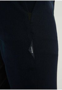 Navyblauwe broeken van gestructureerde stof, met een diagonale naad, een klein zwart logo-label en een taps toelopend ontwerp.