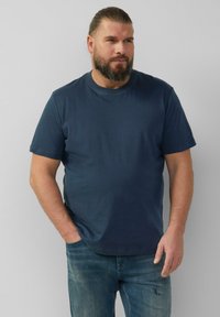 T-shirt in cotone blu navy con maniche corte, scollatura rotonda e vestibilità comoda. Abbinato a jeans blu sbiaditi, leggermente strappati al ginocchio.