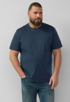 T-shirt en coton bleu marine à manches courtes, col rond et coupe décontractée. Associé à un jean bleu délavé, légèrement usé au genou.