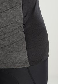 Šedý a černý atletický top s texturovaným povrchem, zdobený zakřivenými liniemi, bočním zipem a materiálem odvádějícím vlhkost.