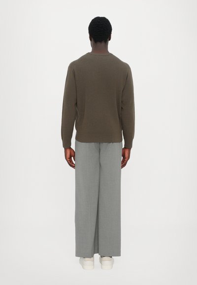 Pruun kudumispullover tekstuurse mustriga, kombineeritud heledate hallide laiade pükstega ja valgete tossudega. Vaade seljalt.