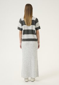 Striped knit sweater in gray and black with short sleeves, paired with a long, light gray ribbed skirt. The outfit features soft textures and a relaxed fit.