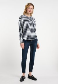Dlhý rukáv, pruhovaná košeľa v námořníckej modrej a bielej farbe s vreckom na hrudi, skombinovaná s tmavomodrými slim-fit džínsami a čiernymi mokasínami.
