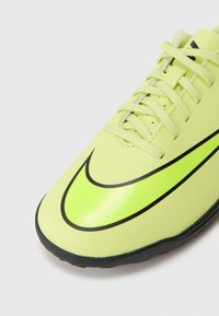 Limegrønn idrettssko med en glanset svart swoosh, teksturert overmateriale, seks snørehull og en gummisåle for bedre grep.
