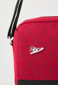 Borsa in tessuto rosso con base nera, con un accento a forma di scarpa e un motivo in rilievo con il numero 23.
