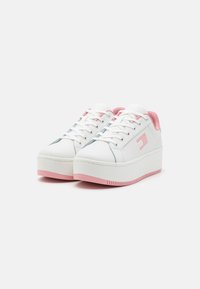 White platform sneakers with pink accents. Smooth synthetic material, round toe, lace-up front, and embossed logo detail on the side.