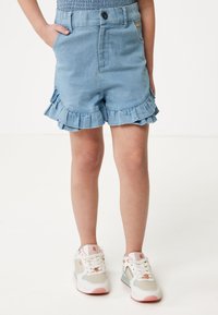 Ljust blå denimshorts med volangkanter, en framficka och knäppning, ihop med vita sneakers med pastellfärger.