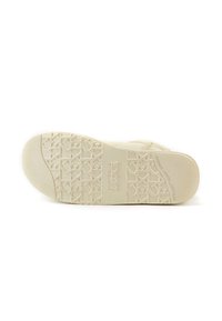 Suela de una sandalia en blanco roto, con goma texturizada que presenta un patrón geométrico y una marca en relieve, ofreciendo agarre y durabilidad.