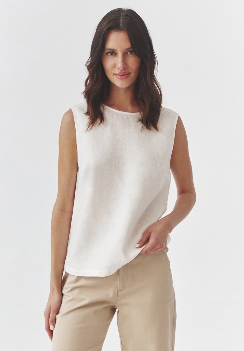 Ľahký, bezrukávový ľanový top v off-white farbe, s okrúhlym výstrihom a voľným strihom, skombinovaný so béžovými nohavicami. Hladká textúra.