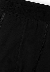 Czarne bokserki z tkaniny z teksturowanym paskiem w talii, na którym wytłoczono słowo "SZACUNEK". Gładka powierzchnia z wzmocnionymi szwami.