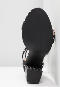 Sandale à talon noir à pois avec talon bloc, vue de la semelle sur fond blanc anguleux.