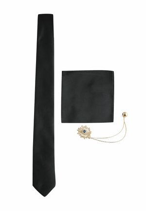 Schwarze schmale Krawatte, passende schwarze Einstecktuch, und goldene Blumenanstecknadel mit blauem Zentrum und Kette auf weißem Hintergrund.