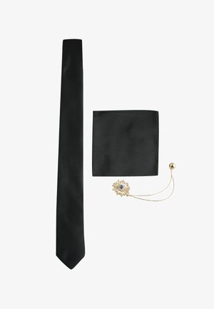 Schwarze schmale Krawatte, passende schwarze Einstecktuch, und goldene Blumenanstecknadel mit blauem Zentrum und Kette auf weißem Hintergrund.