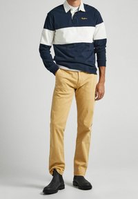 Polo à manches longues rayé bleu marine et blanc avec un col, associé à un pantalon beige et des bottines noires. Design simple, coupe décontractée.