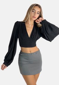 Cropped top nero a pieghe con scollatura a V profonda e maniche lunghe fluide, abbinato a una mini gonna grigia attillata con una cintura stretta.