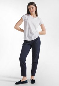 Bílé tričko s krátkým rukávem, námořnicky modré slim-fit kalhoty a tmavě modré slip-on boty s volným střihem a hladkou texturou látky.