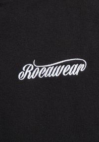 Tessuto nero con un logo ricamato bianco "Rocawear" in un elegante carattere corsivo, su uno sfondo a texture liscia.