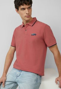 Polo in corallo con colletto e bordi delle maniche blu navy; presenta un piccolo design ricamato di un'auto d'epoca sul petto.
